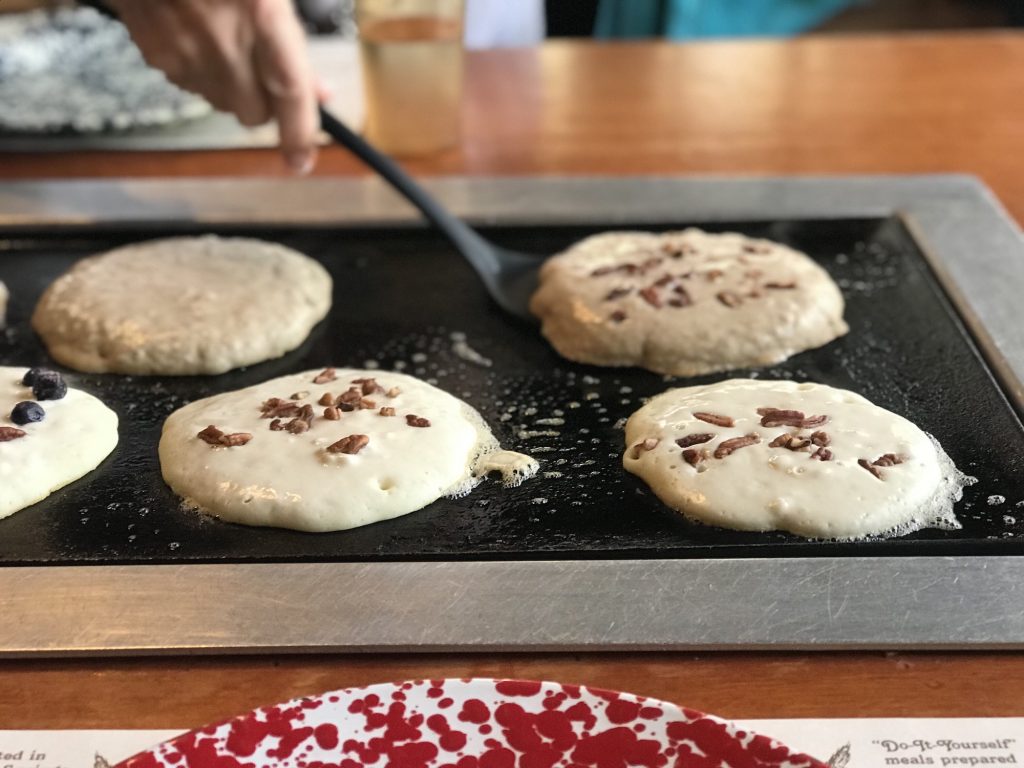 Pancakes are being flipped on a hot griddle and have pecans in them