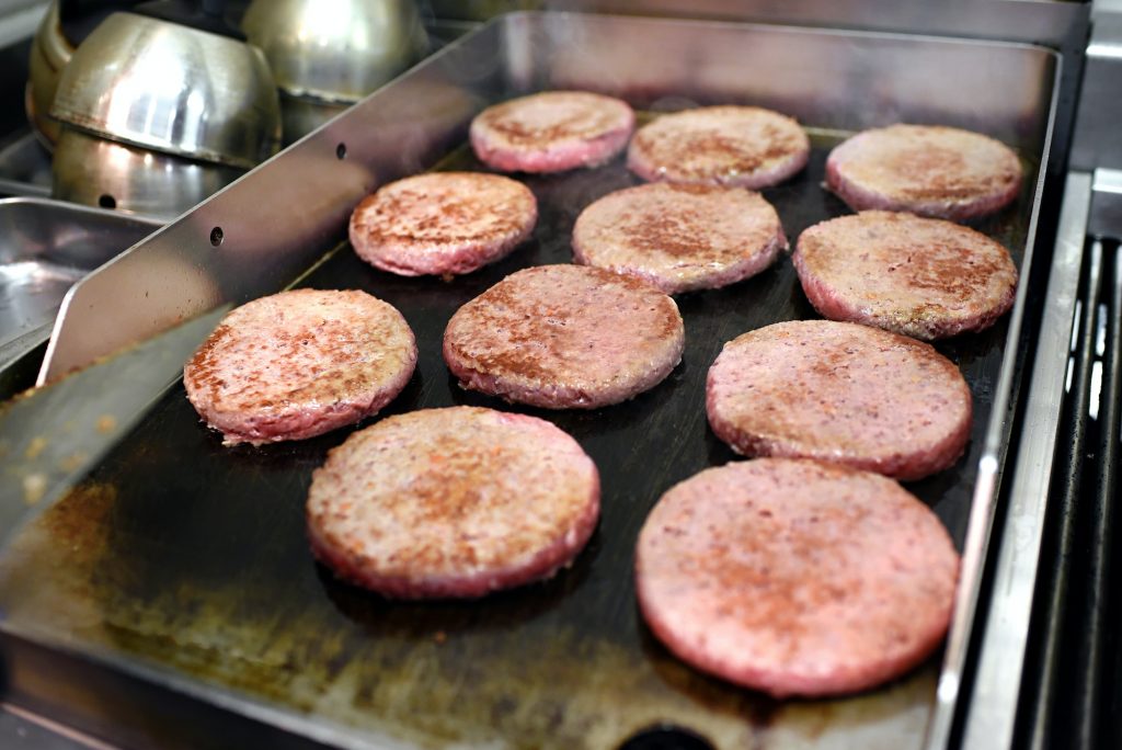 Rows of burger patties cooking on a hot griddle