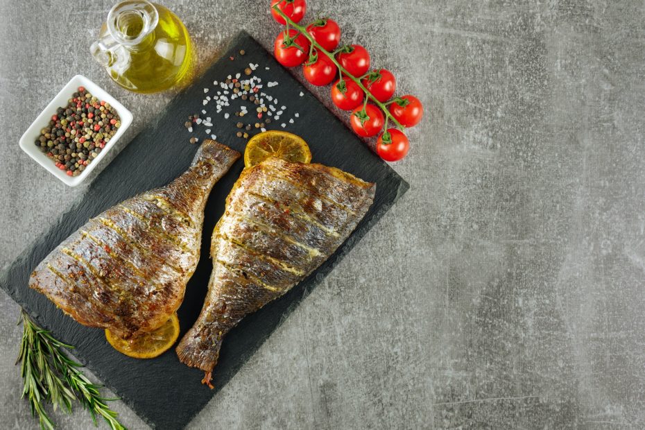 Grilled fish with roasted with lemon and spices on gray background with copy space
