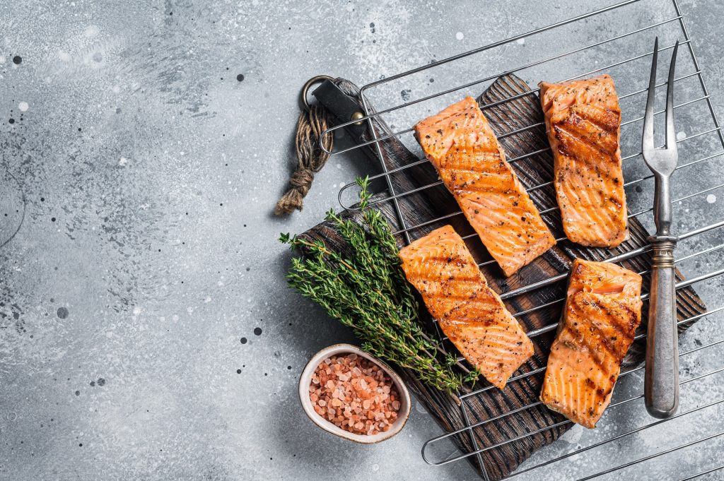 Grilled salmon fillets steaks with salt pepper and herb on grill. Gray background