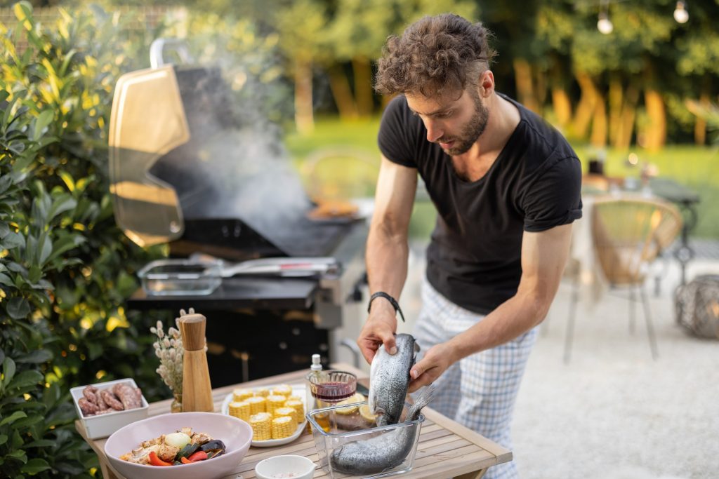 Man cooking fish and vegetables on a grill outdoors